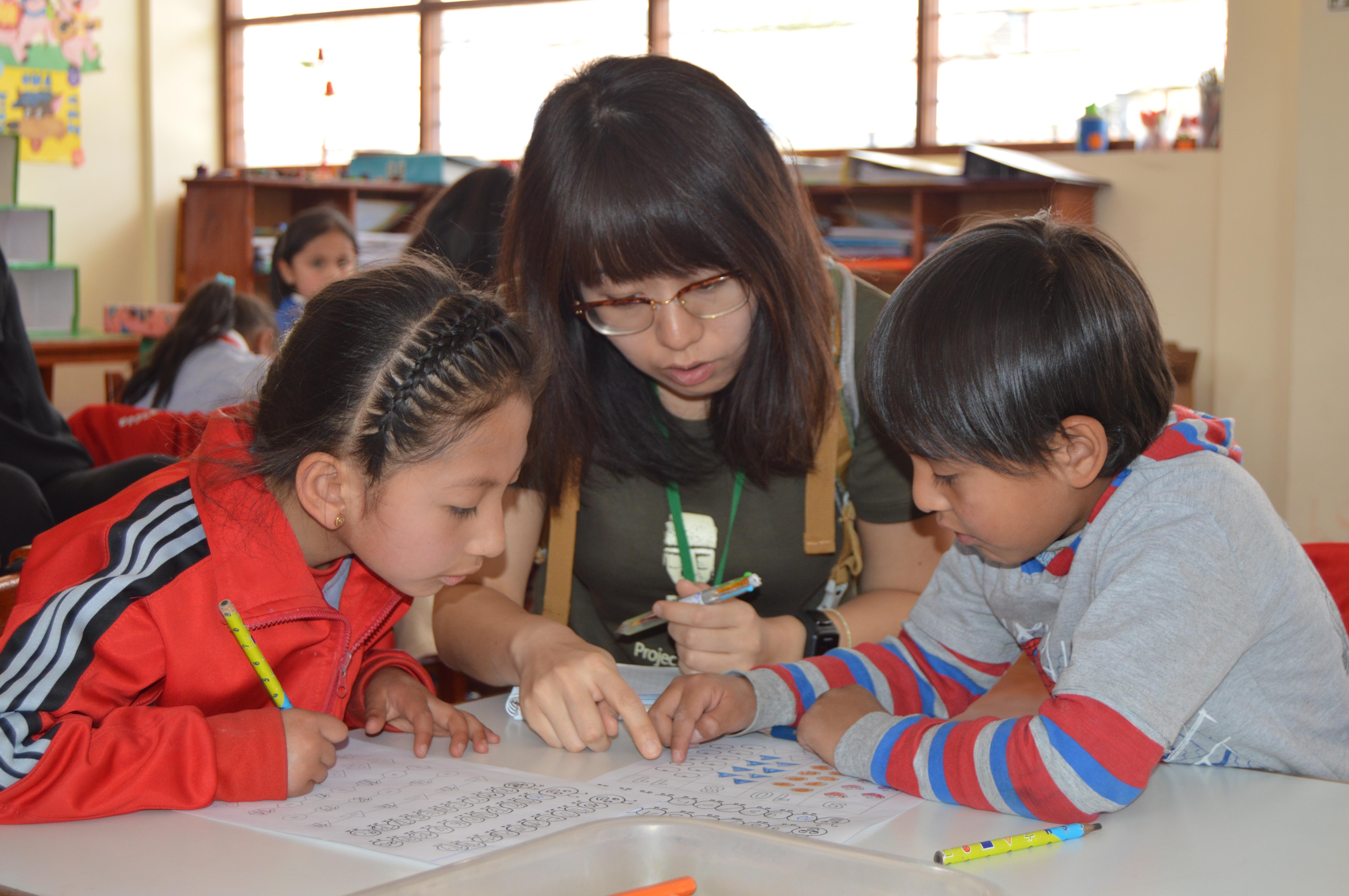 As community volunteer work for teenagers in Peru, a volunteer helps a young girl with an activity. Teenage volunteers doing work with children in Peru, help in the classroom with activities.
